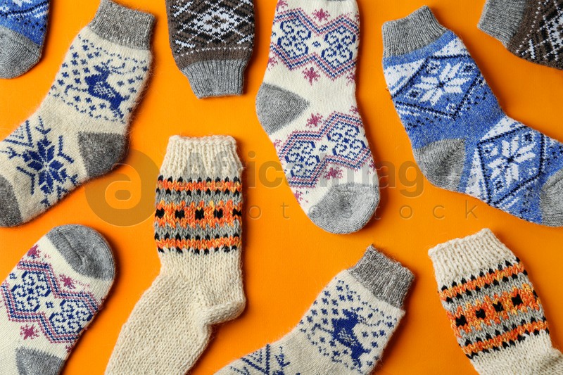 Different knitted socks on orange background, flat lay. Winter clothes