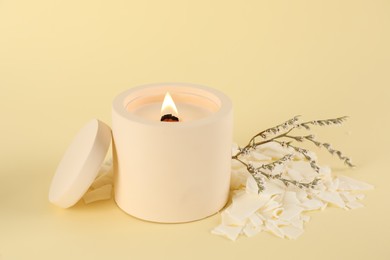 Burning soy candle, wax flakes and statice twig on beige background