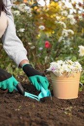 Photo of Woman in gardening gloves preparing soil for flowers transplantation outdoors, closeup