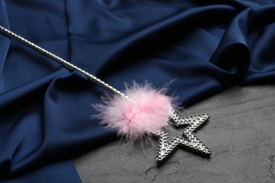Beautiful silver magic wand with feather and blue fabric on black table