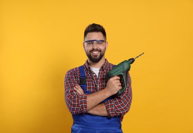 Young worker in uniform with power drill on yellow background