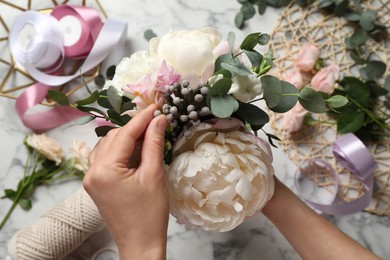 Florist creating beautiful bouquet at white marble table, top view