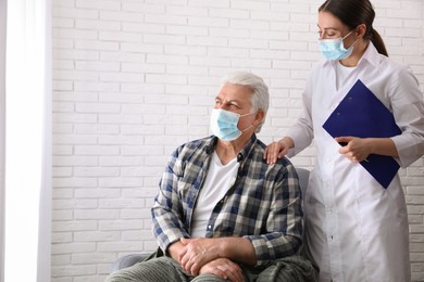 Doctor taking care of senior woman in protective mask at nursing home. Space for text