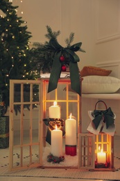 Wooden decorative lanterns with burning candles near Christmas tree in room