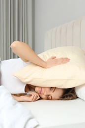 Sleepless woman covering head with pillow in bed at home