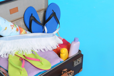 Open vintage suitcase with different beach objects packed for summer vacation on light blue background, closeup