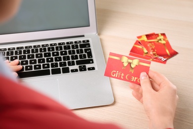 Woman with gift card and laptop at wooden table, closeup