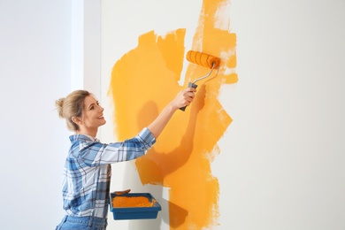 Happy woman painting wall indoors, space for text. Home repair