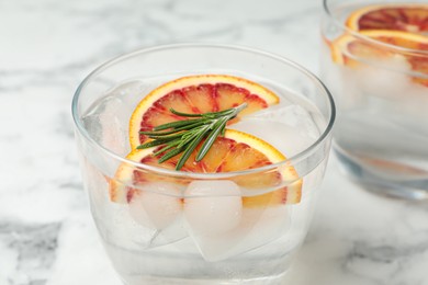 Delicious refreshing drink with sicilian orange and rosemary on white marble table, closeup