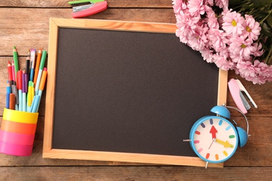 Blackboard, stationery, alarm clock and flowers on wooden table, flat lay with space for text. Teacher's Day