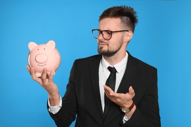 Confused businessman with piggy bank on light blue background
