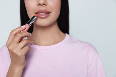 Photo of Young woman applying nude lipstick on gray background, closeup
