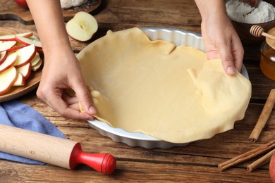 Woman putting dough for apple pie into baking dish at wooden table, closeup