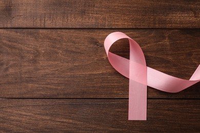 Photo of Pink ribbon on wooden table, top view with space for text. Breast cancer awareness concept