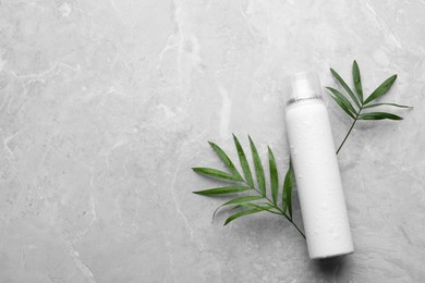 Photo of Dry shampoo spray and green leaves on light grey table, flat lay. Space for text