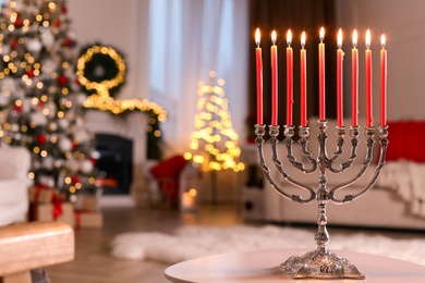 Silver menorah on white table in room with fireplace and Christmas decorations. Hanukkah symbol
