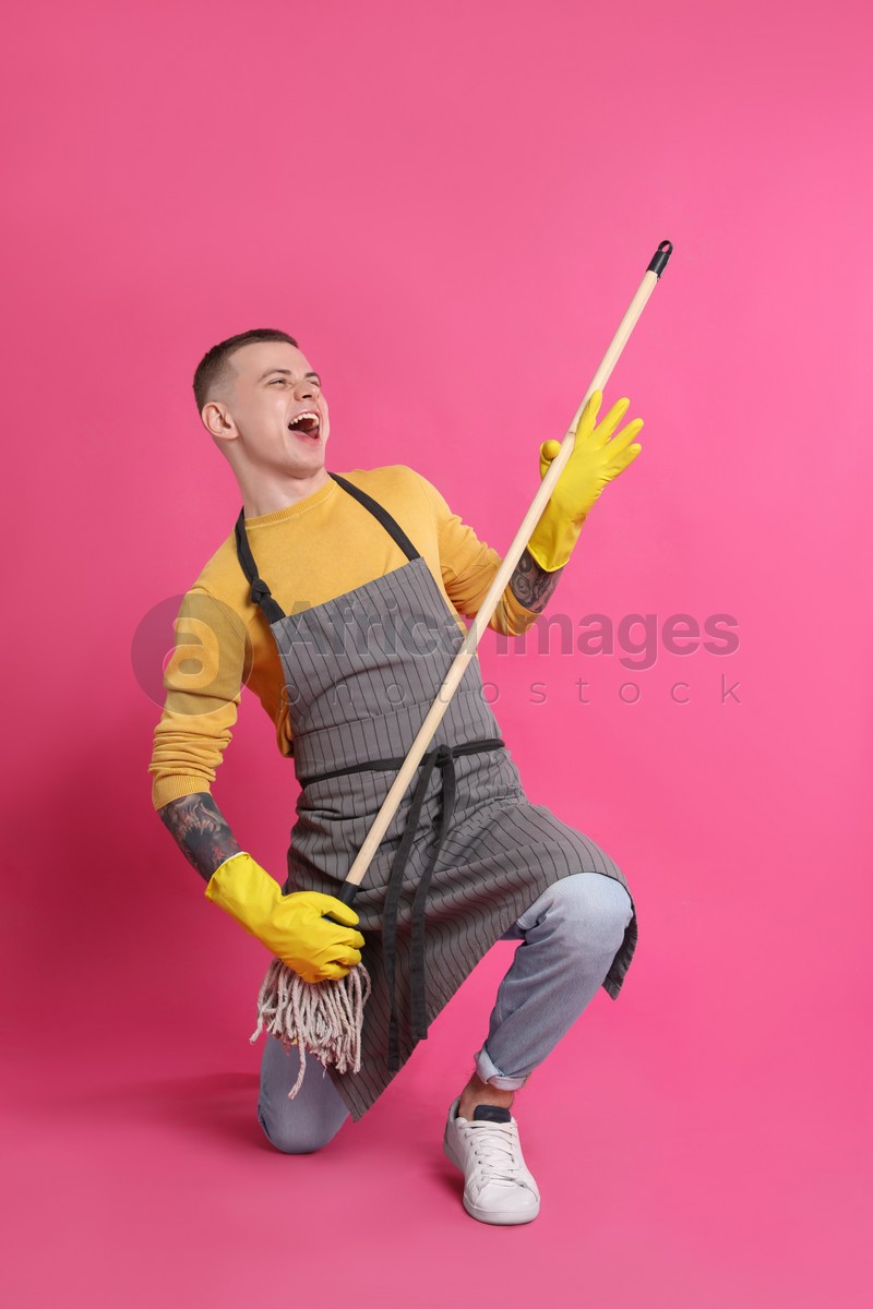 Photo of Handsome young man with mop singing on pink background
