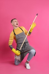 Handsome young man with mop singing on pink background