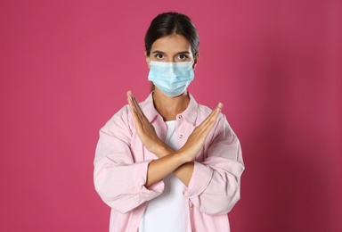 Woman in protective mask showing stop gesture on pink background. Prevent spreading of coronavirus