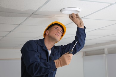 Electrician with screwdriver repairing ceiling lamp indoors