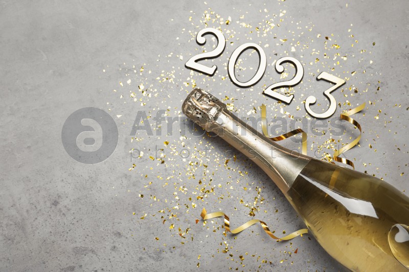 Bottle of sparkling wine, festive decor and number 2023 on grey background, flat lay with space for text. Happy New Year