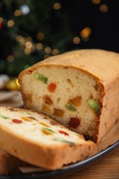 Delicious cake with candied fruits on wooden table against Christmas lights, closeup
