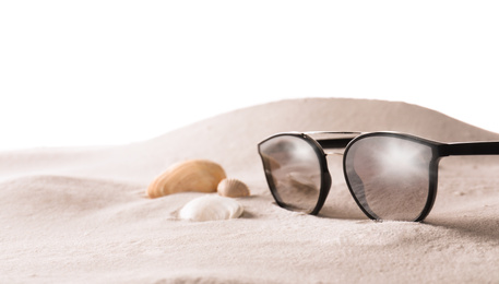Stylish sunglasses and shells on sand against white background. Space for text