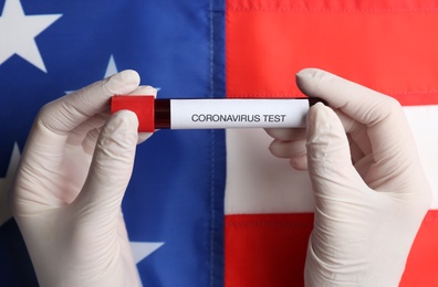 Scientist holding test tube with blood sample over American flag, closeup. Coronavirus pandemic in USA