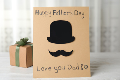 Greeting card with phrase HAPPY FATHER'S DAY I LOVE YOU DAD and gift box on white wooden table indoors