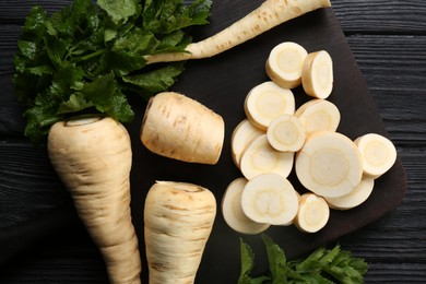 Photo of Whole and cut parsnips on black wooden table, flat lay