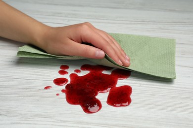 Woman wiping spilled jam with paper towel on wooden table, closeup