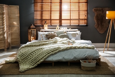 Cozy bedroom interior with knitted blanket and cushions
