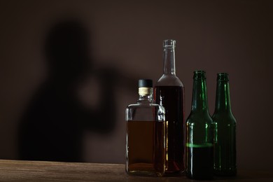 Alcoholic drinks on wooden table against brown wall with shadow of addicted man