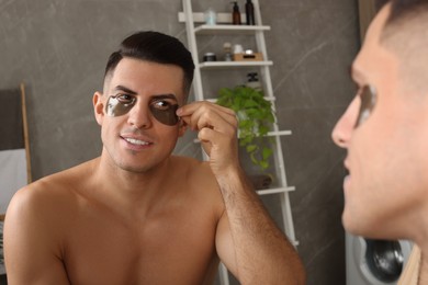 Man applying dark under eye patches near mirror at home