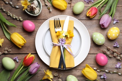 Festive Easter table setting with painted eggs and floral decor on wooden background, flat lay
