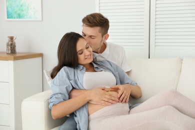 Young husband and his pregnant wife resting on sofa at home