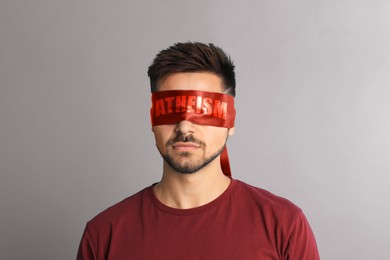 Image of Man wearing red blindfold with word Atheism on light grey background