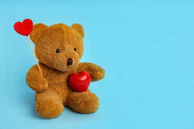 Cute teddy bear with red hearts on light blue background, space for text. Valentine's day celebration