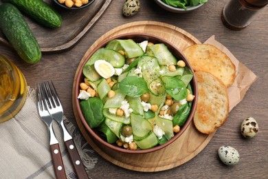 Delicious cucumber salad and toasted bread served on wooden table, flat lay