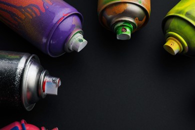 Used cans of spray paints on black background, closeup with space for text. Graffiti supplies