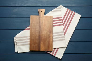 Striped kitchen towel and cutting board on blue wooden table, top view