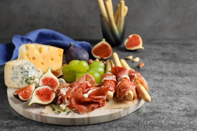 Photo of Board with delicious figs, cheese, grapes and bread with proscuitto on grey table