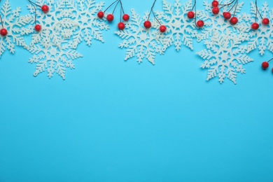 Beautiful decorative snowflakes and red berries on light blue background, flat lay. Space for text