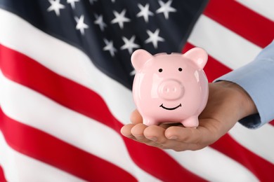 Woman holding piggy bank against American flag, closeup. Space for text
