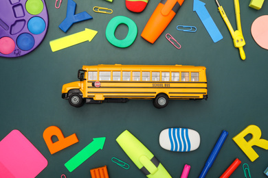 Yellow school bus and stationery on green background, flat lay. Transport for students