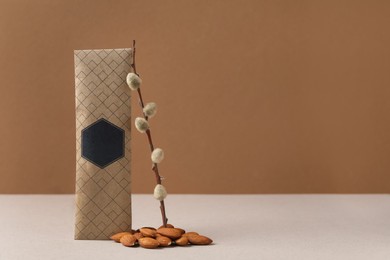 Scented sachet, pussy willow branch and almonds on grey table against brown background, space for text