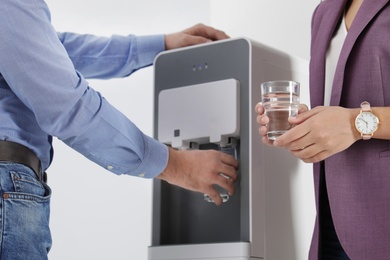 Employees taking glasses of water from cooler in office, closeup