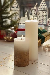 Beautiful burning candles with Christmas decor on white wooden table near window