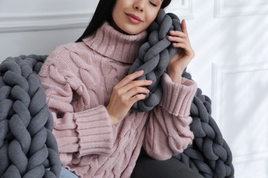Photo of Young woman with chunky knit blanket on sofa at home, closeup