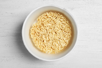 Photo of Cup of instant noodles on white wooden background, top view